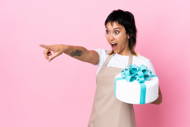 Uruguayischer Konditor, der einen großen Kuchen über lokalisiertem rosa Zeigefinger zur Seite hält