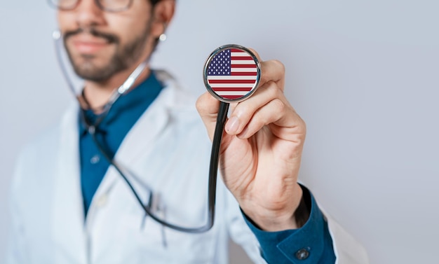 USA-Flagge auf Stethoskop. Arzt hält Stethoskop mit USA-Flagge. Arzt zeigt Stethoskop mit USA-Flagge
