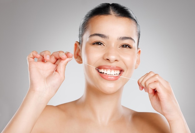 Usa hilo dental para flexionar tu sonrisa Foto de estudio de una atractiva joven que usa hilo dental contra un fondo gris