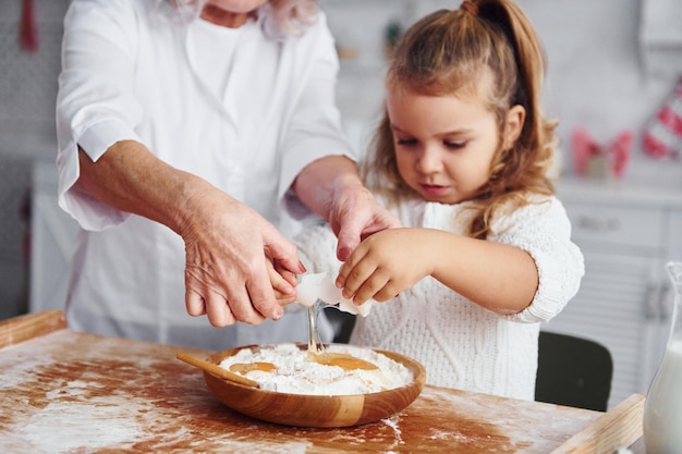 Usa huevos La abuela mayor con su nieta cocina dulces para Navidad en la cocina