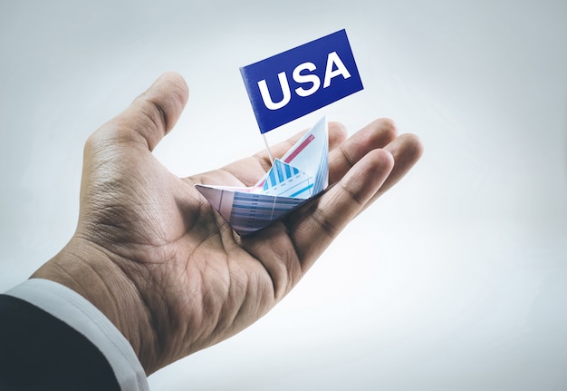 USA-Nachricht auf Flagge mit Boot aus Papiergraph in Geschäftsmannhand