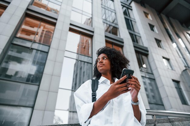 Usa telefone mulher afro-americana em boas roupas está ao ar livre na cidade durante o dia