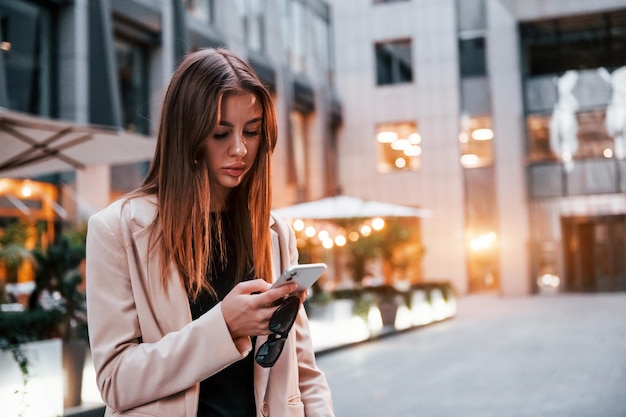 Usa el teléfono Hermosa joven europea está al aire libre en la ciudad durante el día