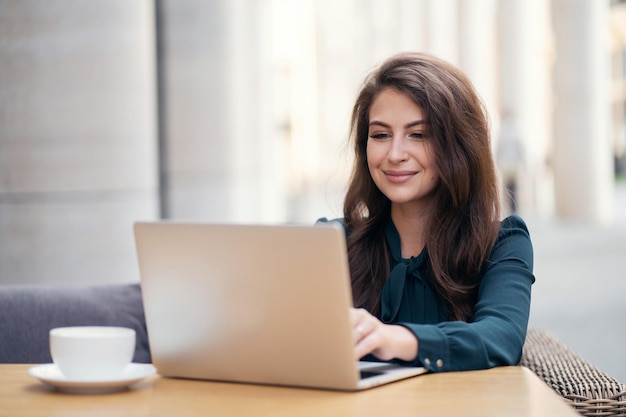 Usa um laptop e escreve uma mensagem para o cliente Uma mulher em um vestido formal trabalha em um café