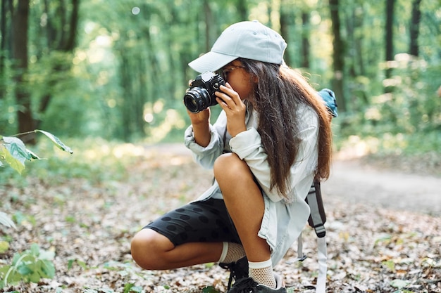 Usando a câmera profissional A garota está na floresta durante o dia de verão descobrindo novos lugares