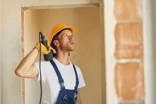 Usando a ferramenta Jovem trabalhando de uniforme na construção durante o dia