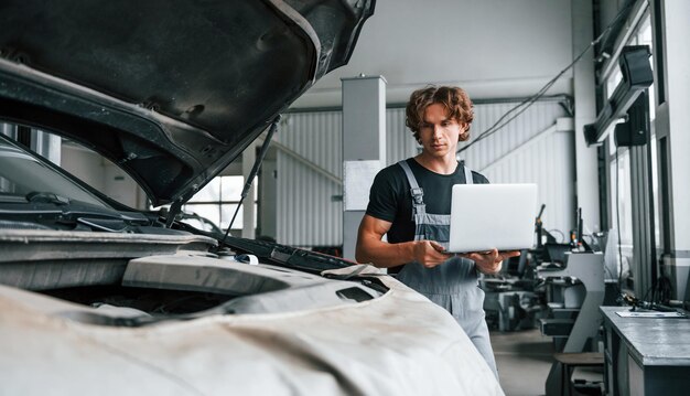 Usando computadora Hombre adulto en uniforme de color gris trabaja en el salón del automóvil