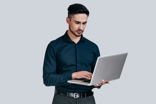 Usando computadora portátil. Hombre joven guapo en camisa trabajando en equipo portátil