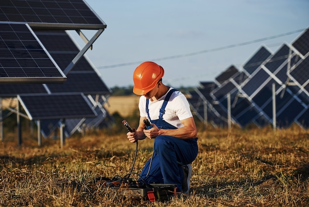 Usando equipamento especial. trabalhador masculino com uniforme azul ao ar livre com baterias solares em dia ensolarado.