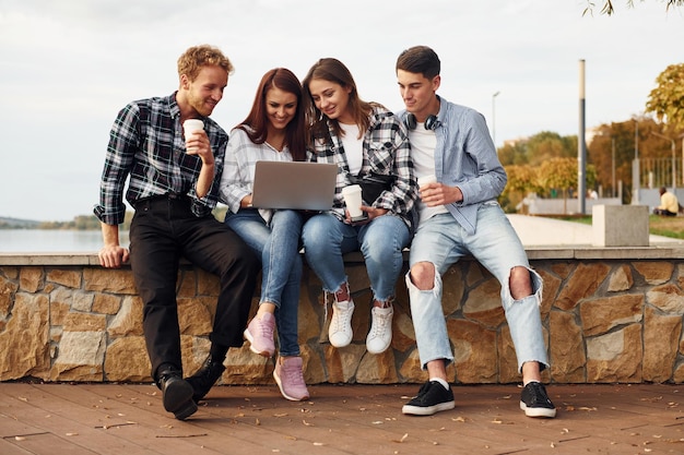 Usando laptop Grupo de jóvenes amigos alegres que están al aire libre divirtiéndose juntos