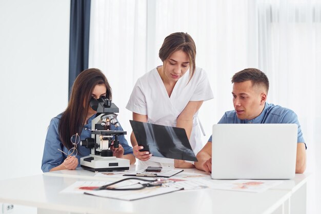 Usando microscópio Grupo de jovens médicos está trabalhando juntos no escritório moderno