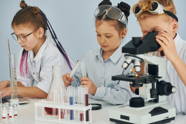 Usando microscopio Los niños con batas blancas juegan a los científicos en el laboratorio usando equipos