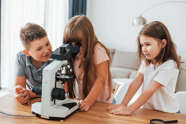 Usando microscopio Niños divirtiéndose juntos en la sala doméstica durante el día