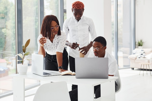 Usando o mesmo laptop para o projeto Grupo de empresários afro-americanos trabalhando juntos no escritório