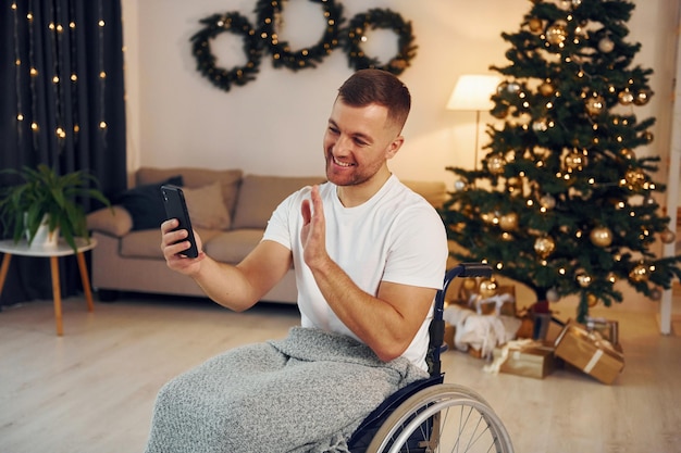 Usando o smartphone para se comunicar com as pessoas O ano novo está chegando Homem com deficiência em cadeira de rodas está em casa