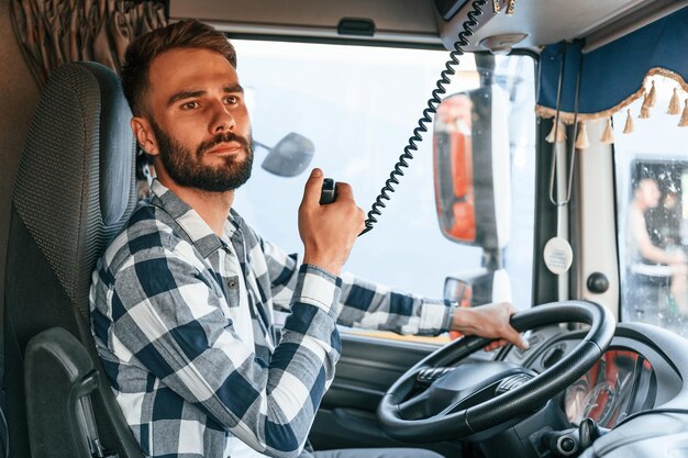 Usando la radio, el joven camionero está con su vehículo durante el día.