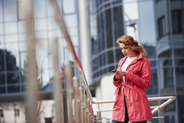 Usando redes sociales. Mujer bonita adulta en abrigo rojo cálido tiene caminar en la ciudad en su tiempo de los fines de semana