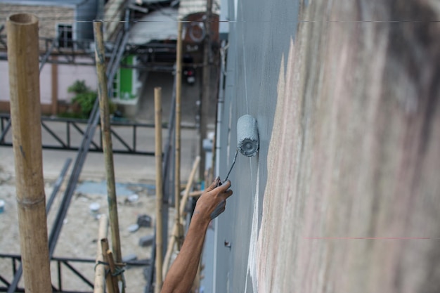 usando un rodillo de pintura para pintar la pared del edificio