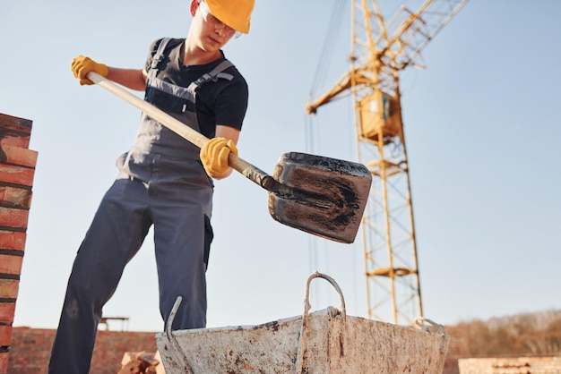 Usando showel Trabalhador da construção em uniforme e equipamento de segurança tem trabalho na construção