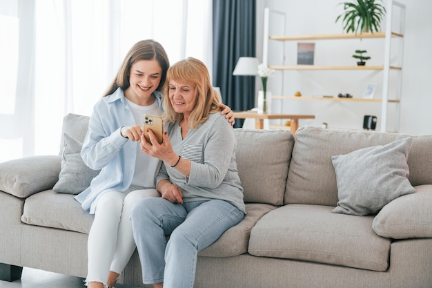 Usando smartphone Mãe e filha estão juntas em casa