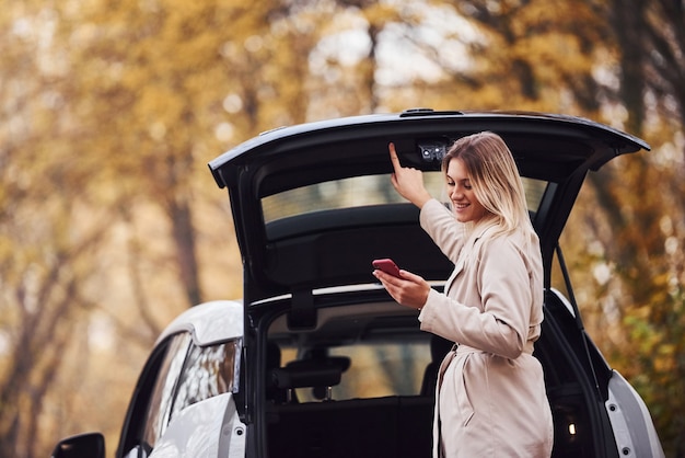 Usando smartphone. menina tem viagem de outono de carro. automóvel novo moderno na floresta.