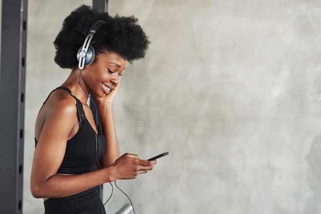 Usando smartphone. retrato de uma garota afro-americana com roupas de ginástica, fazendo uma pausa após o treino