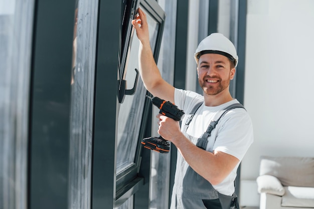 Usando taladro instalando windows Repairman está trabajando en el interior de la habitación moderna