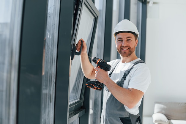 Usando taladro instalando windows Repairman está trabajando en el interior de la habitación moderna