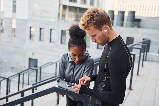 Usando telefone, homem europeu e mulher afro-americana em roupas esportivas treinam juntos