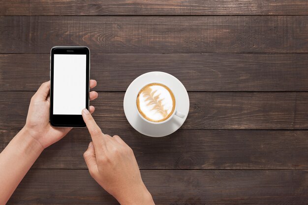 Usando el teléfono inteligente al lado de café en la mesa de madera