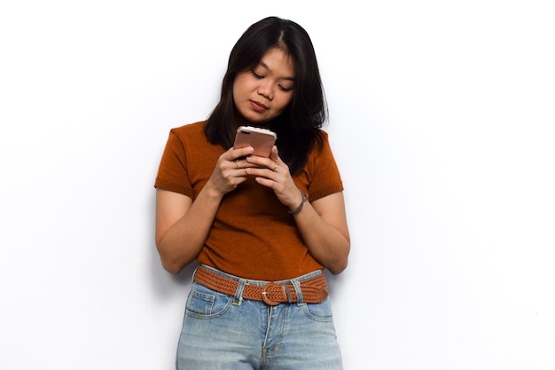 Usando el teléfono inteligente de las mujeres asiáticas hermosas jóvenes visten camisa naranja aislada sobre fondo blanco