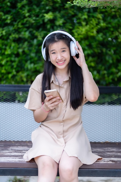 Foto usando un teléfono inteligente sosteniendo un dispositivo de teléfono móvil con auriculares inalámbricos blancos y escuchando