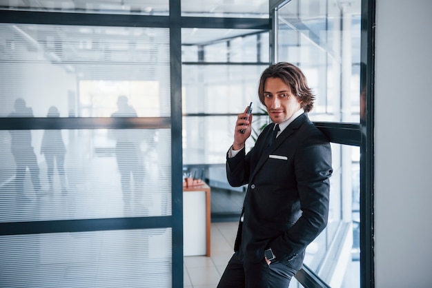 Usando el teléfono. Retrato de joven empresario guapo en traje negro y corbata.