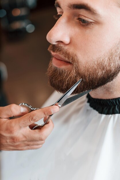 Usando tesouras Homem está visitando barbearia moderna estilo moderno