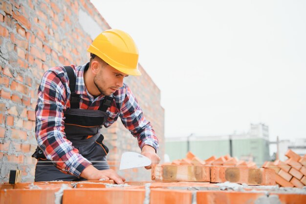 Foto usando tijolos jovem trabalhador da construção civil de uniforme está ocupado no prédio inacabado