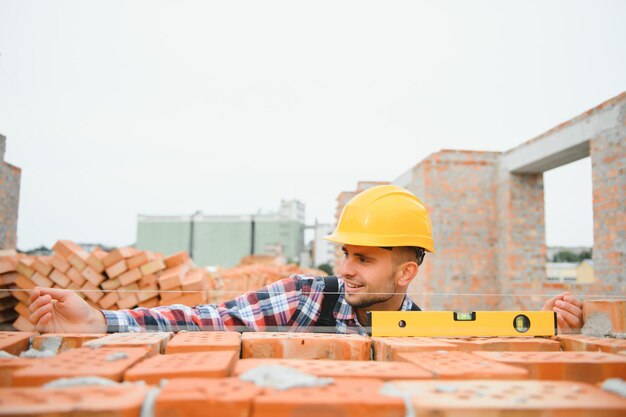 Usando tijolos Jovem trabalhador da construção civil de uniforme está ocupado no prédio inacabado