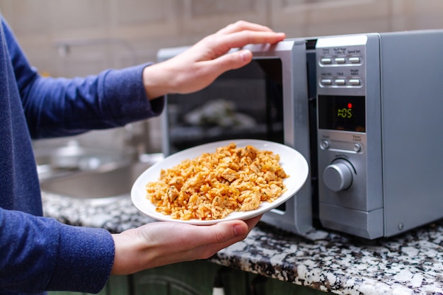 Foto usando um microondas para aquecer um prato de pilau caseiro para almoçar em casa. comida quente