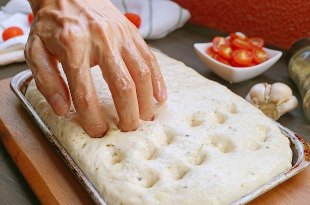 Usando las yemas de los dedos para crear hoyuelos en la masa para hornear pan italiano Focaccia Genovese