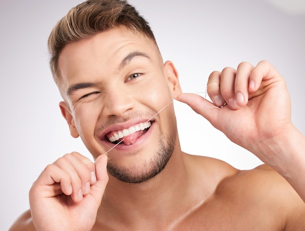 Usar hilo dental te mantiene fresco Foto de estudio de un joven que se pasa el hilo dental sobre un fondo gris