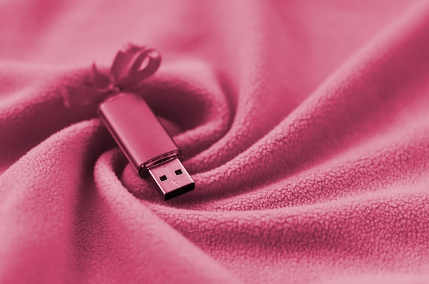 USB-Flash-Speicherkarte mit Schleife liegt auf einer Decke aus weichem und pelzigem Fleece-Stoffbild, das in Viva getönt ist