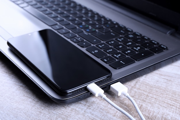 USB-Kabel, Ladegerät, Aufladen, Laden und Datenübertragung des Mobiltelefons, Smartphone mit Laptop auf Holzboden, Tisch Draufsicht einstecken