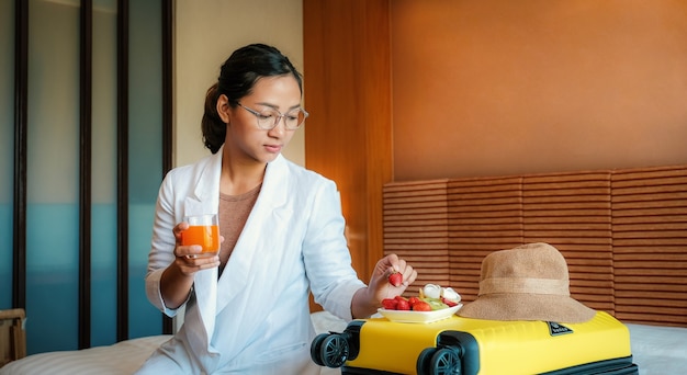 Usinesswoman isst Obst und trinkt Orangensaft auf dem Bett im Luxushotelzimmer gesundes Essenskonzept