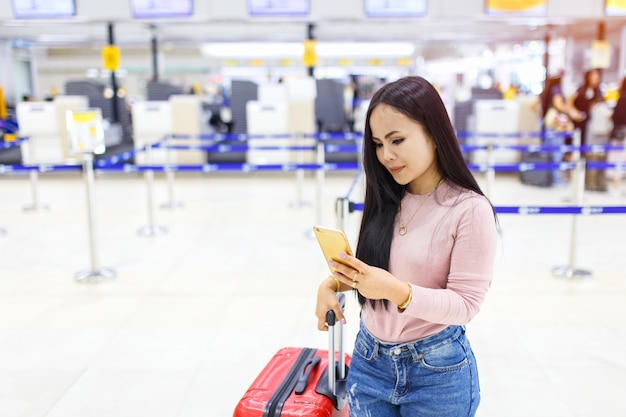 Uso asiático de la mujer del teléfono móvil delante de la verificación línea aérea en línea aérea en el aeropuerto internacional.