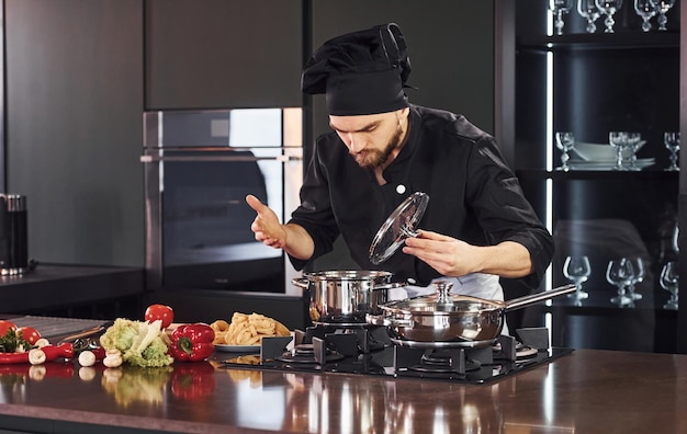 Uso del equipo Cocinero profesional joven en uniforme trabajando en la cocina con verduras