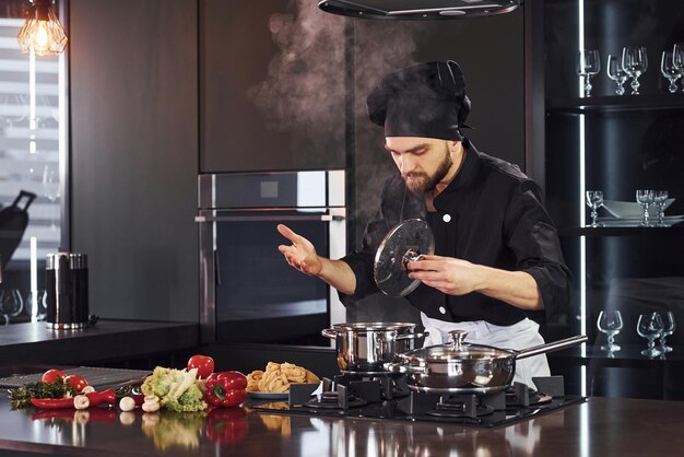 Uso del equipo Cocinero profesional joven en uniforme trabajando en la cocina con verduras