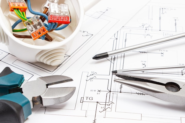 Foto uso de herramientas metálicas para obras caja eléctrica con cables de colores conectados y diagramas de plan de vivienda con instalación eléctrica concepto de casa de construcción