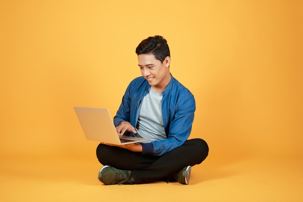 Uso del hombre asiático de la computadora portátil contra el fondo de color naranja