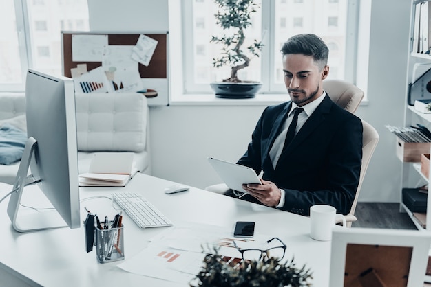 Uso de tecnologías modernas en el trabajo. Hombre joven guapo en traje completo con tableta digital