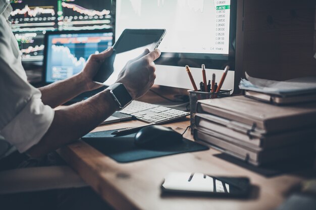 Uso de tecnologías modernas en el trabajo. Primer plano de joven empresario sosteniendo tableta digital mientras está sentado en el escritorio en la oficina creativa