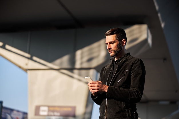 Usuário de smartphone masculino em pé ao ar livre sozinho durante o dia